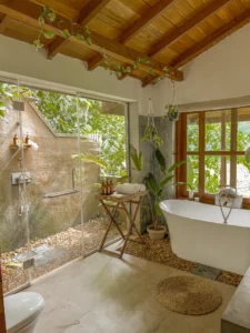 White tub inside a bathroom with wooden ceiling and a glass door looking out on a shower surrounded by greenery at the Jungle Loft Galle, one of the best and most unique Airbnb Sri Lanka.