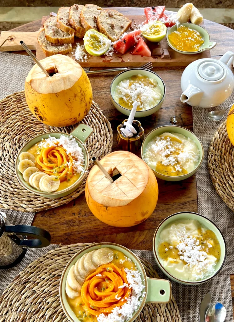 Yellow coconuts, smoothies bowls with fruit shaped as roses and a white pot of tea on a wooden table at the Jungle Loft Galle, one of the best Airbnbs in Sri Lanka.