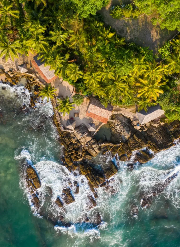 Drone view of palm tree jungle and a hotel set on an outcrop by the water in Tangalle, Sri Lanka.