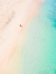 View from above of a girl in a red bikini sitting on Balangan Beach with her legs in the turquoise water, one of the best beaches in Uluwatu, Bali.