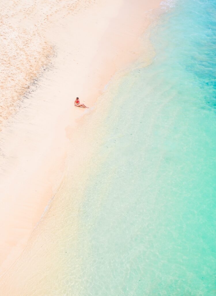 View from above of a girl in a red bikini sitting on Balangan Beach with her legs in the turquoise water, one of the best beaches in Uluwatu, Bali.