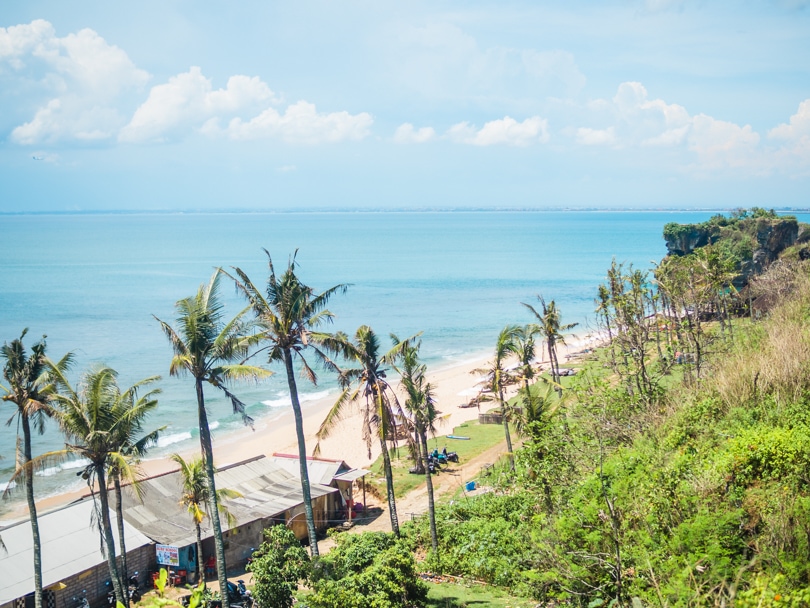 View from the cliff above of Balangan Beach with a warung and a row of palm trees, one of the best beaches in Bali.