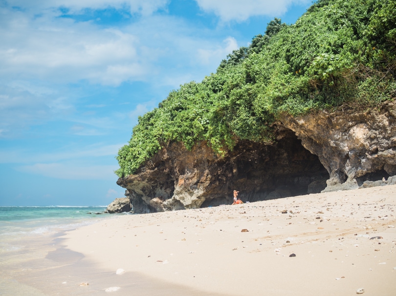 Man standing inside the circular cave covered by greenery on the light sand at Green Bowl Beach - One of the best beaches in Uluwatu.