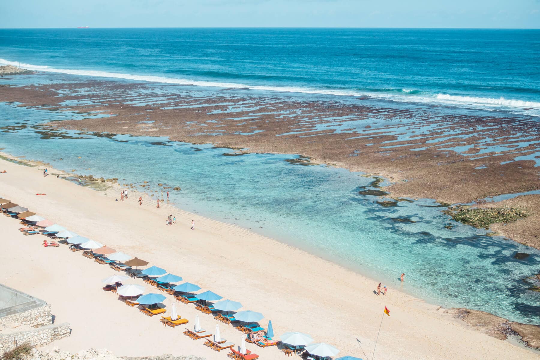 View from above of sun loungers and blue umbrellas along Melasti Beach, one of the best beaches in Uluwatu Bali.