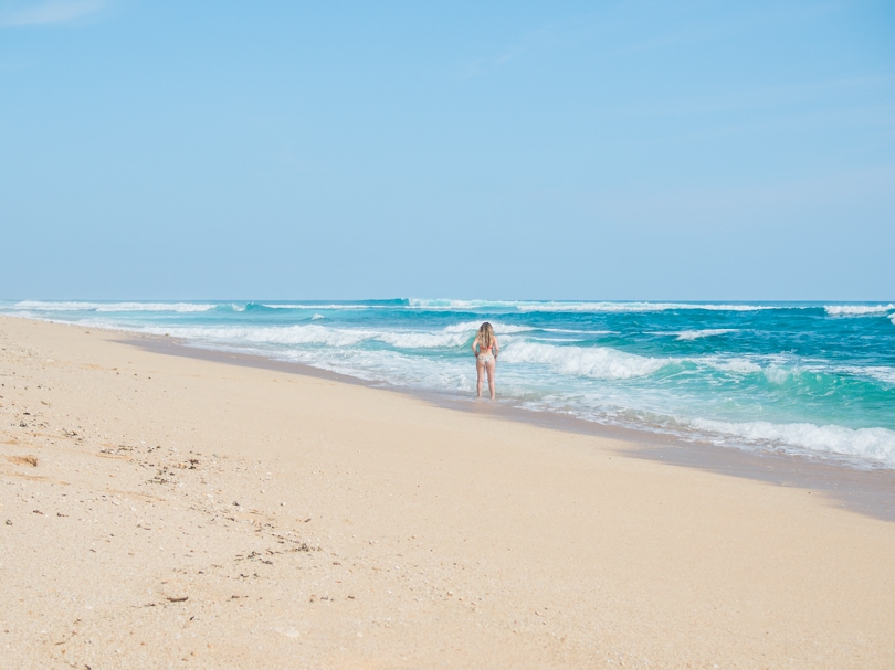 Woman walking on light-sand Nyang Nyang Beach looking out over the waves on a sunny day, one of the best beaches in Uluwatu Bali.