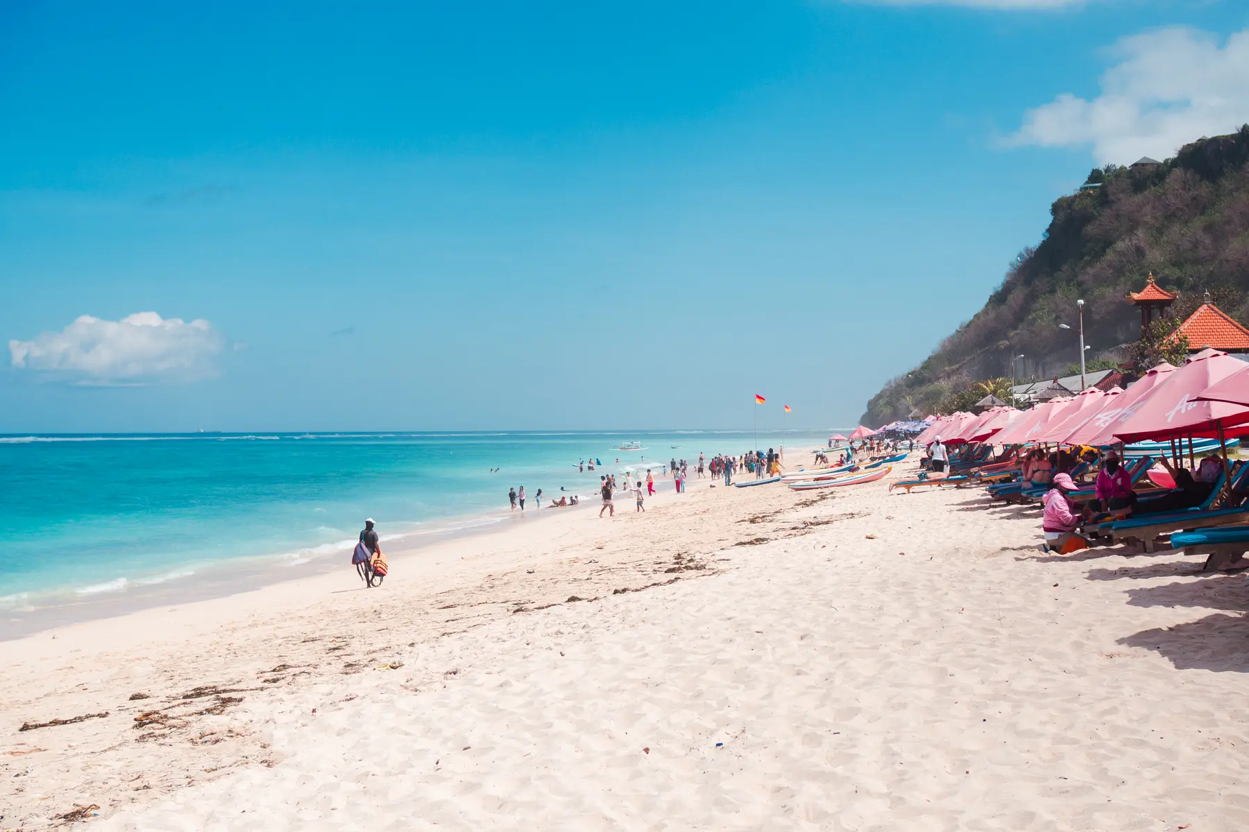 People walking along the white sand Pandawa Beach on a sunny day, one of the best beaches in Uluwatu.