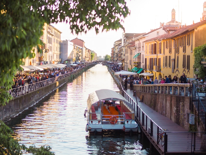 View of a boat on a canal in Navigli with orange houses and lots of people on both sides, during 2 days in Milan.