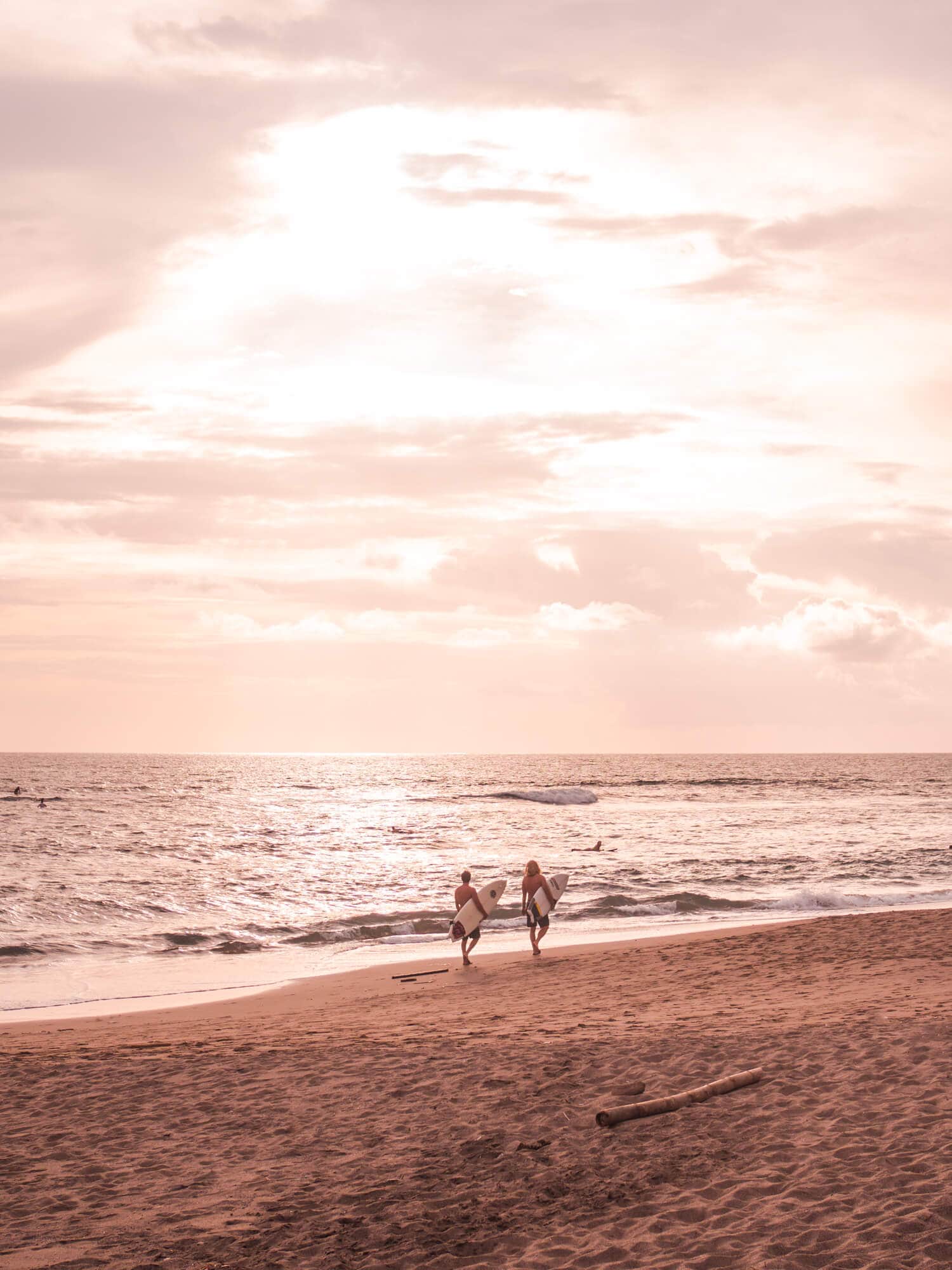 Two surfers carrying their surfboards walking along Batu Bolong Beach in Canggu at sunset.