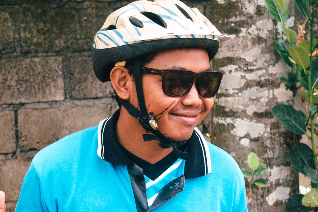 A smiling cycling tour guide wearing a blue shirt and white helmet with a large black and white spider on his cheek.