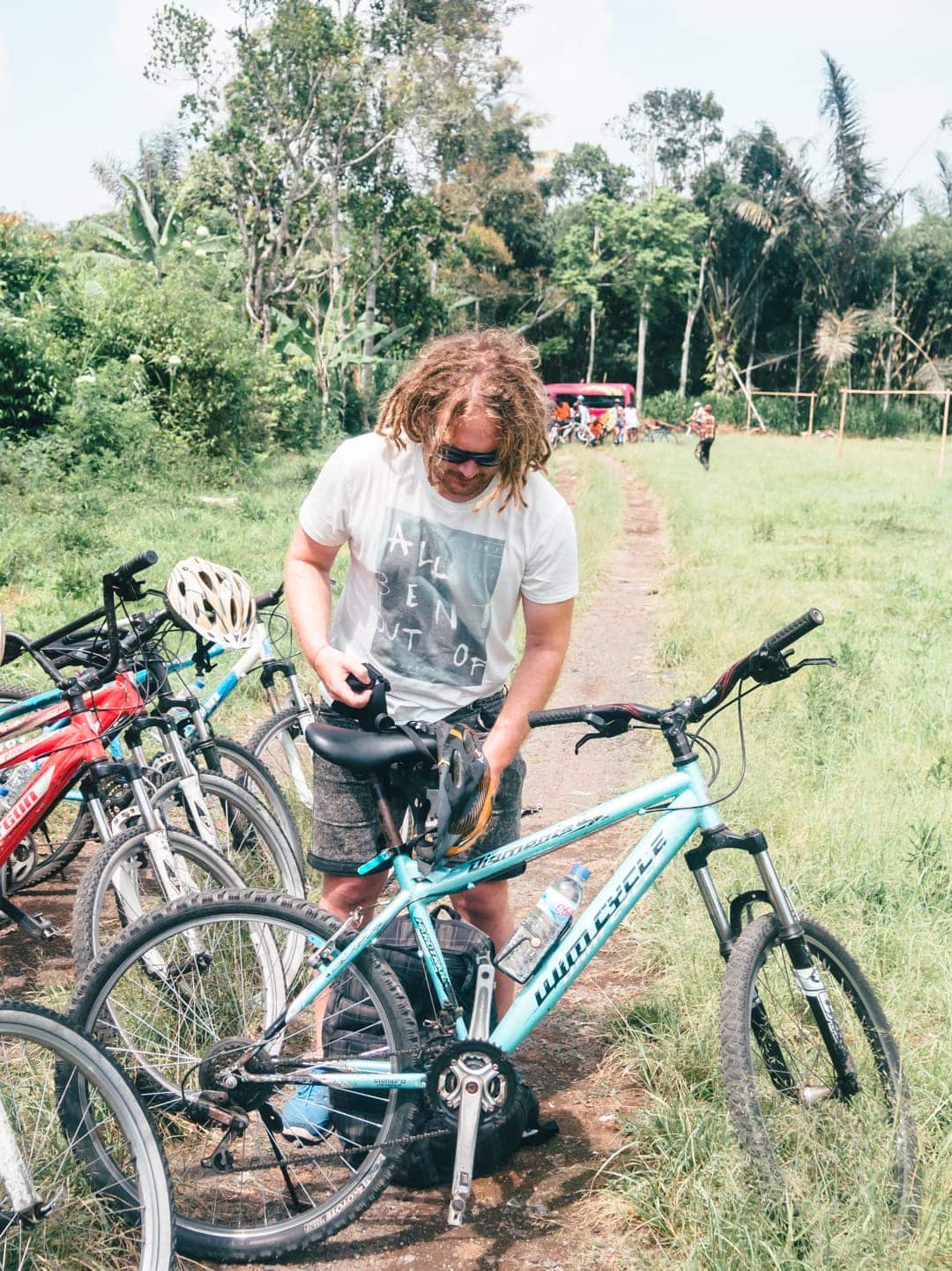 Man with shoulder long, messy hair choosing a turquoise bicycle, almost ready to begin our cycling tour in lush Ubud, Bali.