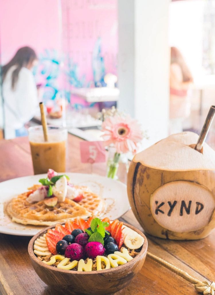 Smoothie bowl, coconut and waffles against a pink wall at Kynd Community Café in Seminyak, a must on any Bali Bucket List.