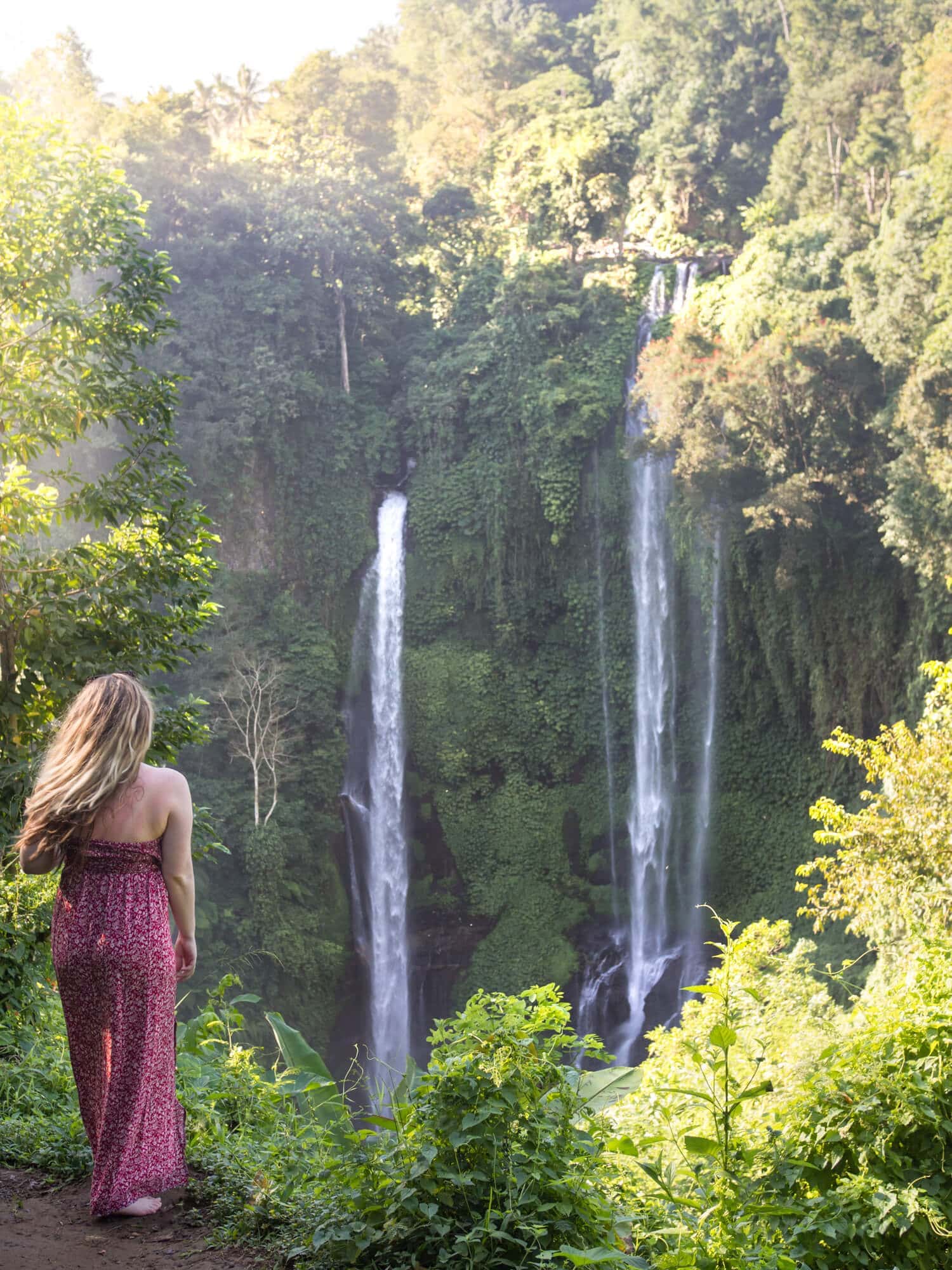 Girl in a red dress in front of the two cascades Sekumpul Waterfall, one of the must see attractions in Bali.