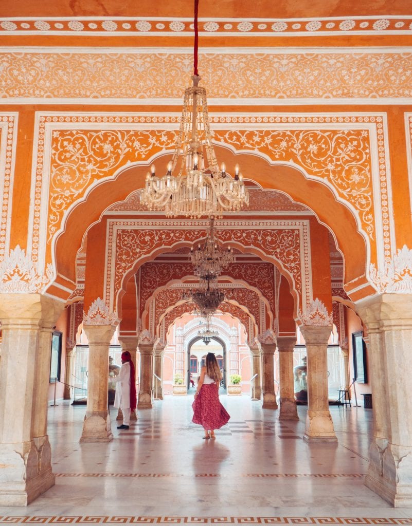 Girl in a pink skirt inside the orange City Palace decorated with columns and white decorations, a must see place during your 2 days in Jaipur.