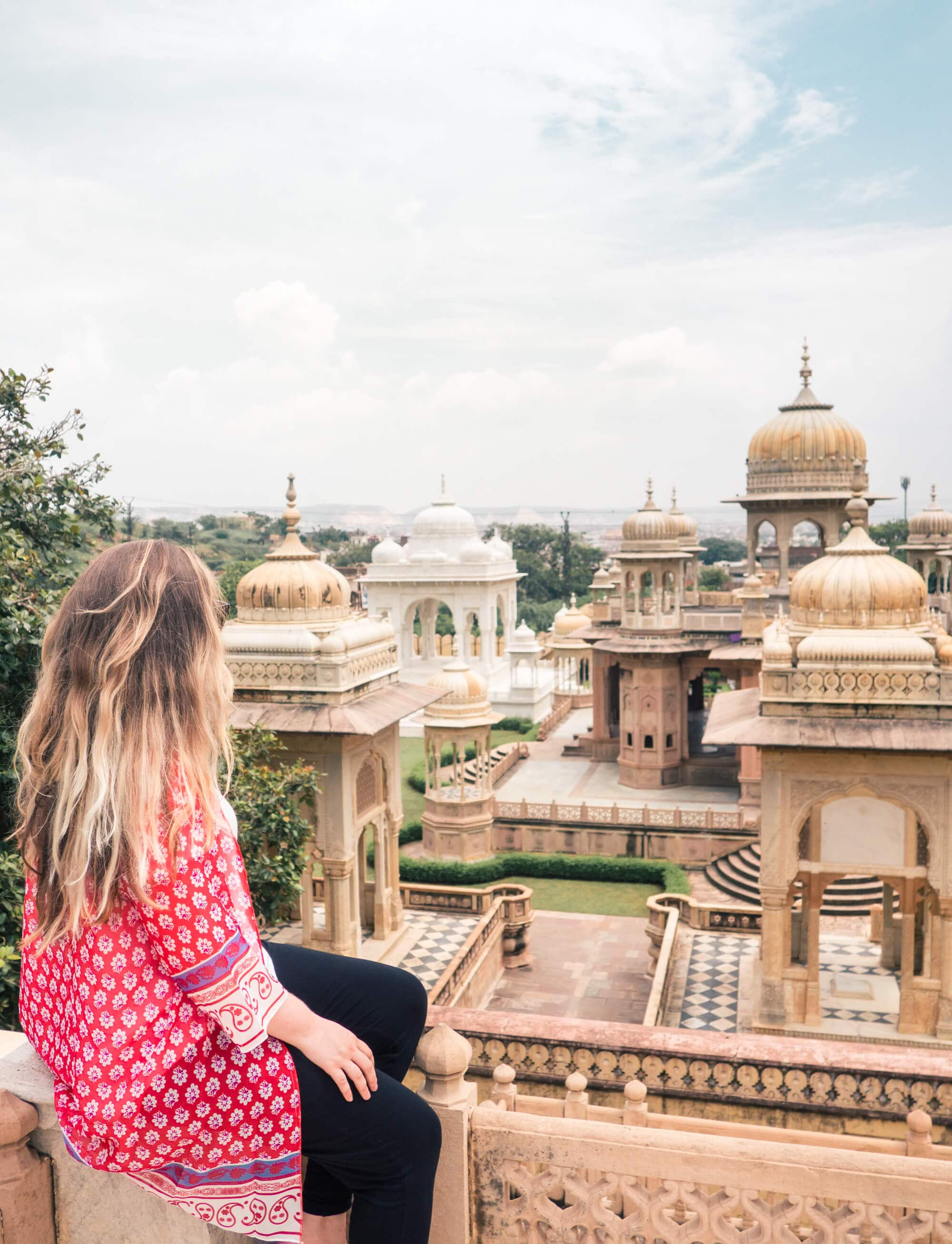 Girl with long hair in a red and white kimono and black pants looking our over the intricate monuments in Gatore Ki Chatriyan, a must during your 2 days in Jaipur.