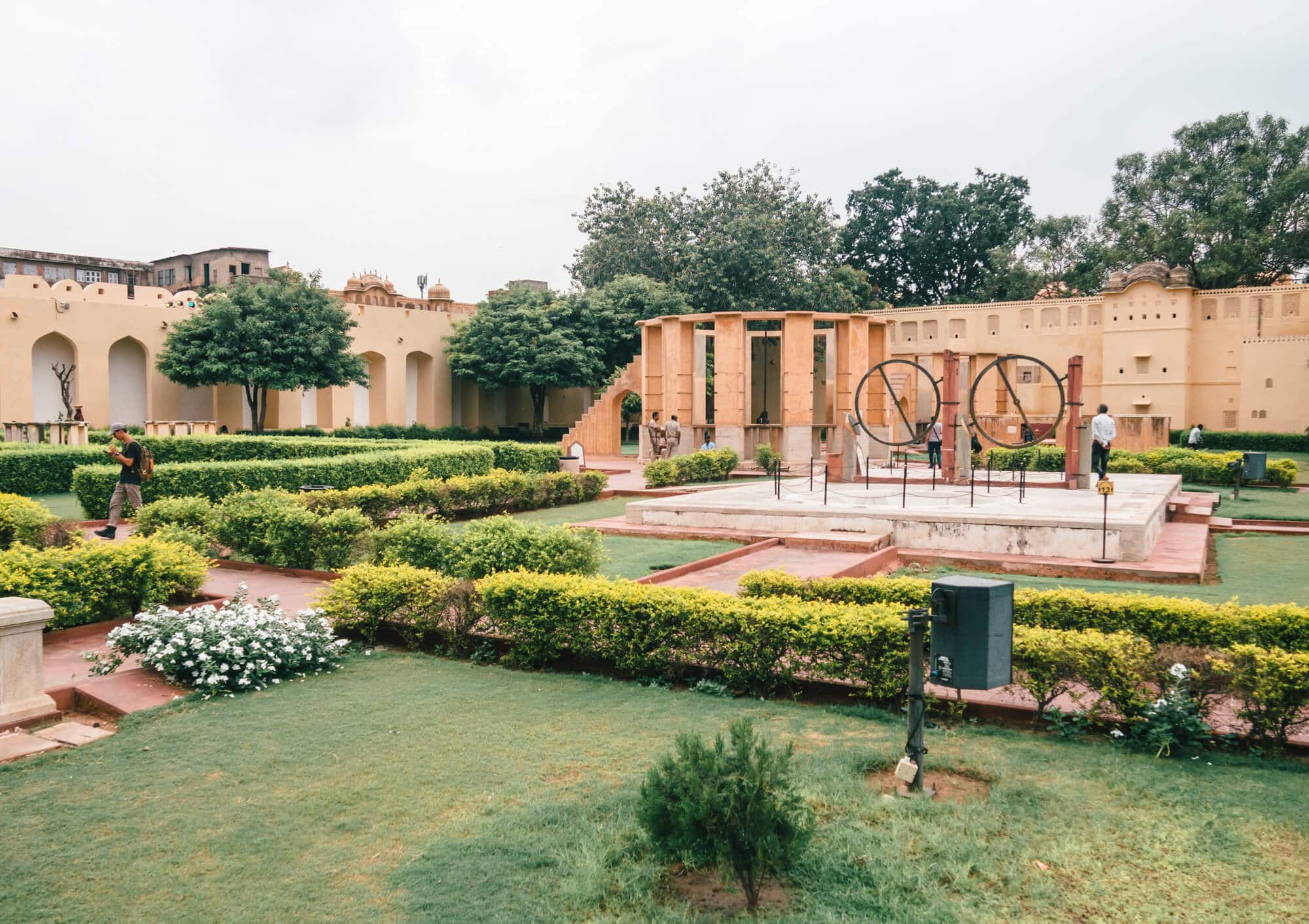View of a garden with green grass, small hedges, beige stone walls and astronomic instruments at Jantar Mantar, a UNESCO World Heritage Site you must include in your 2-day Jaipur itinerary.