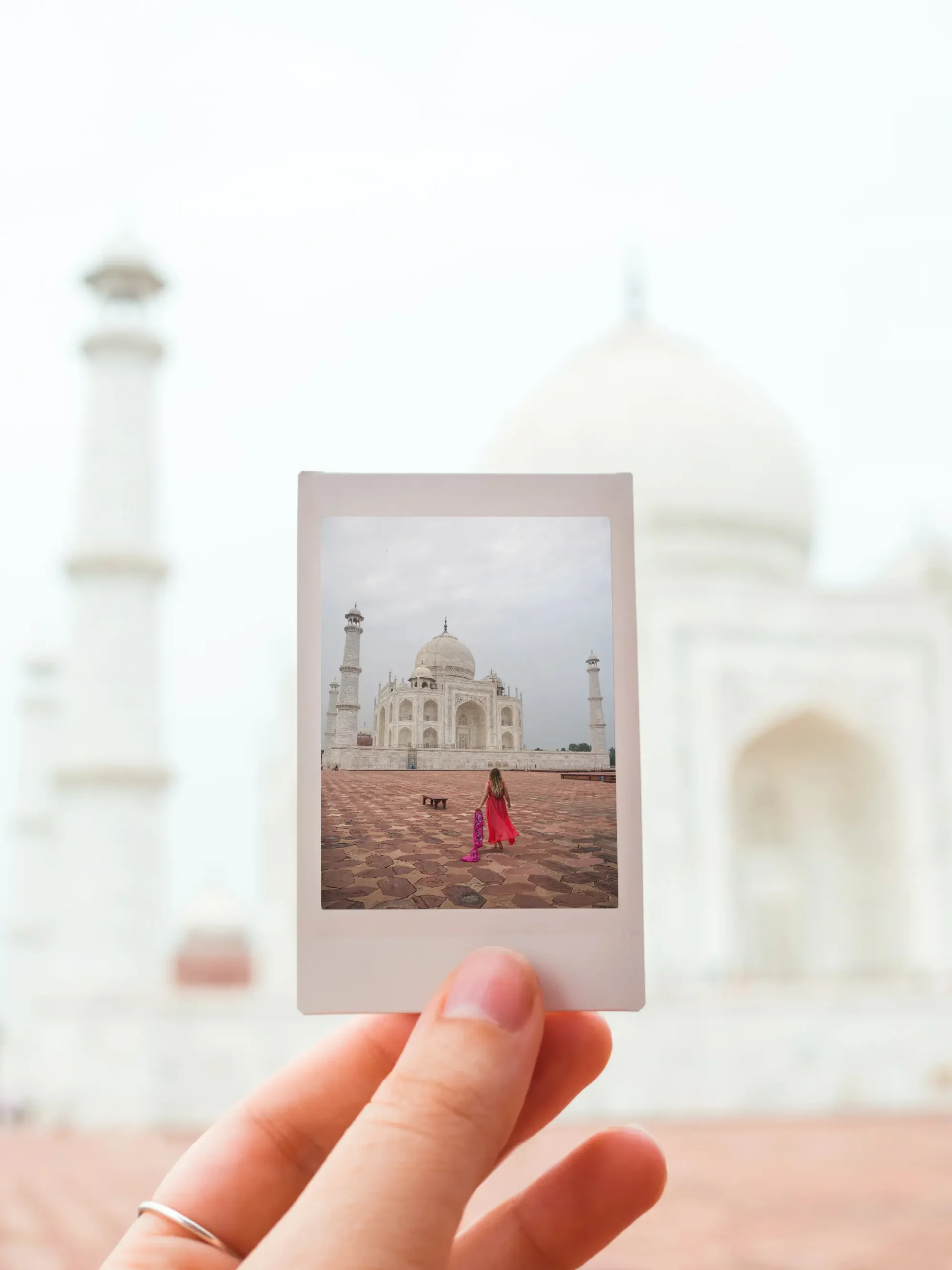 A woman's hand wit a silver ring holding a polaroid of a woman in a pink dress walking towards the white Taj Mahal, photography tips.