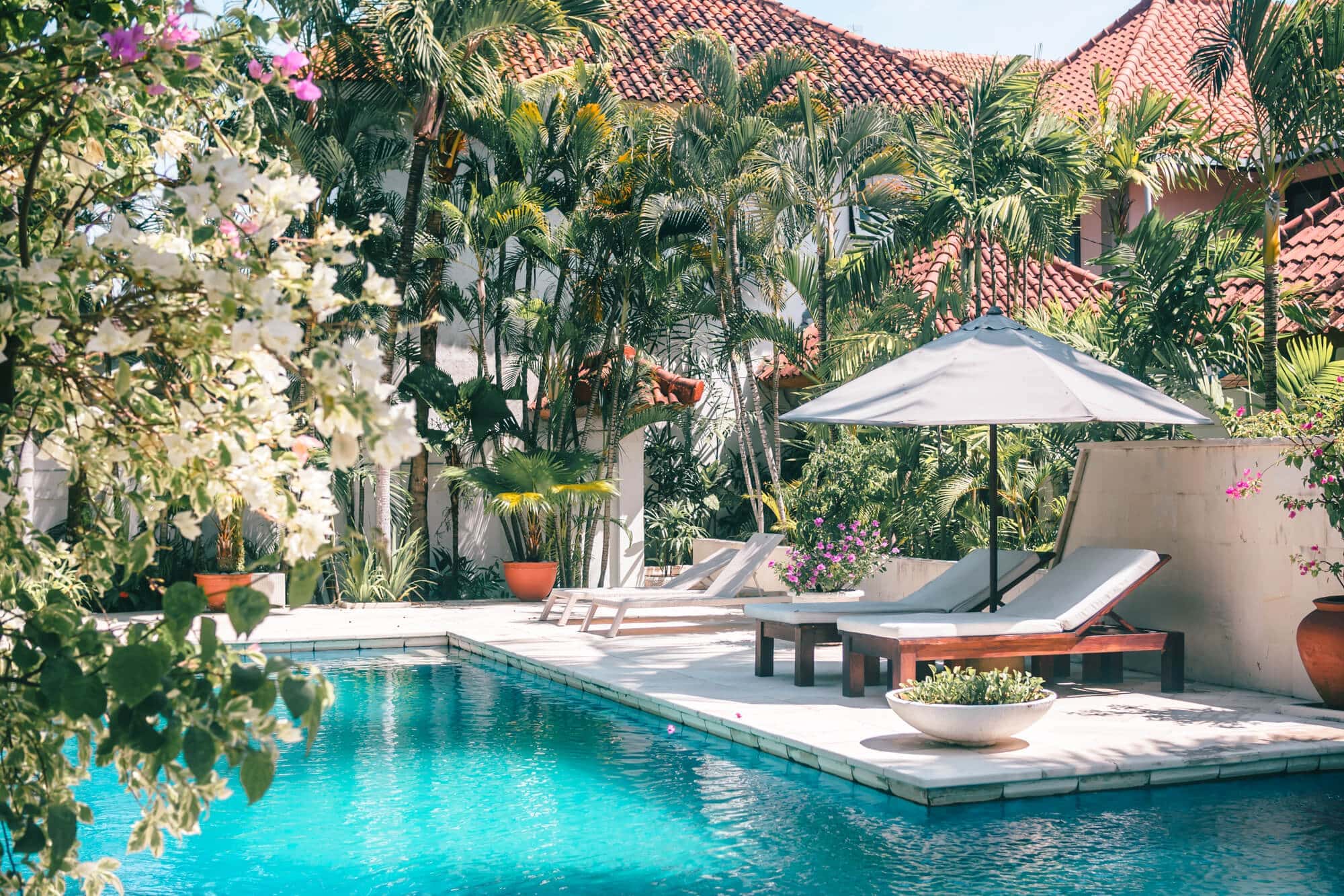 Two sunbeds and a parsol by a turquoise pool surrounded by palms and flowers at a private pool villa, one of the top things to do in Bali.