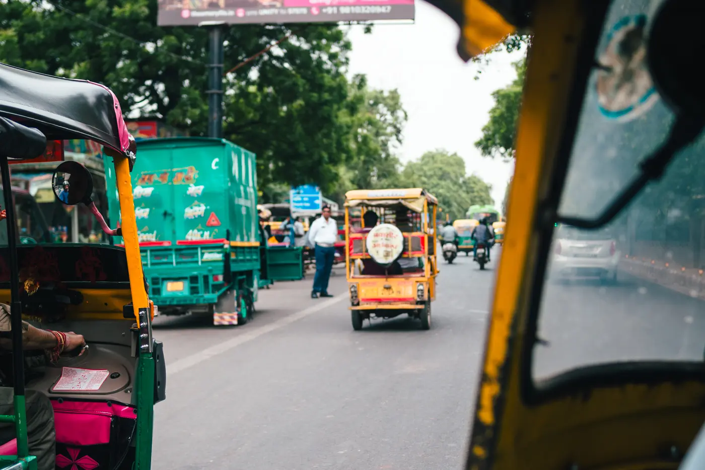 Yellow tuk-tuk next to a green truck on the busy roads of New Delhi India for first-timers.