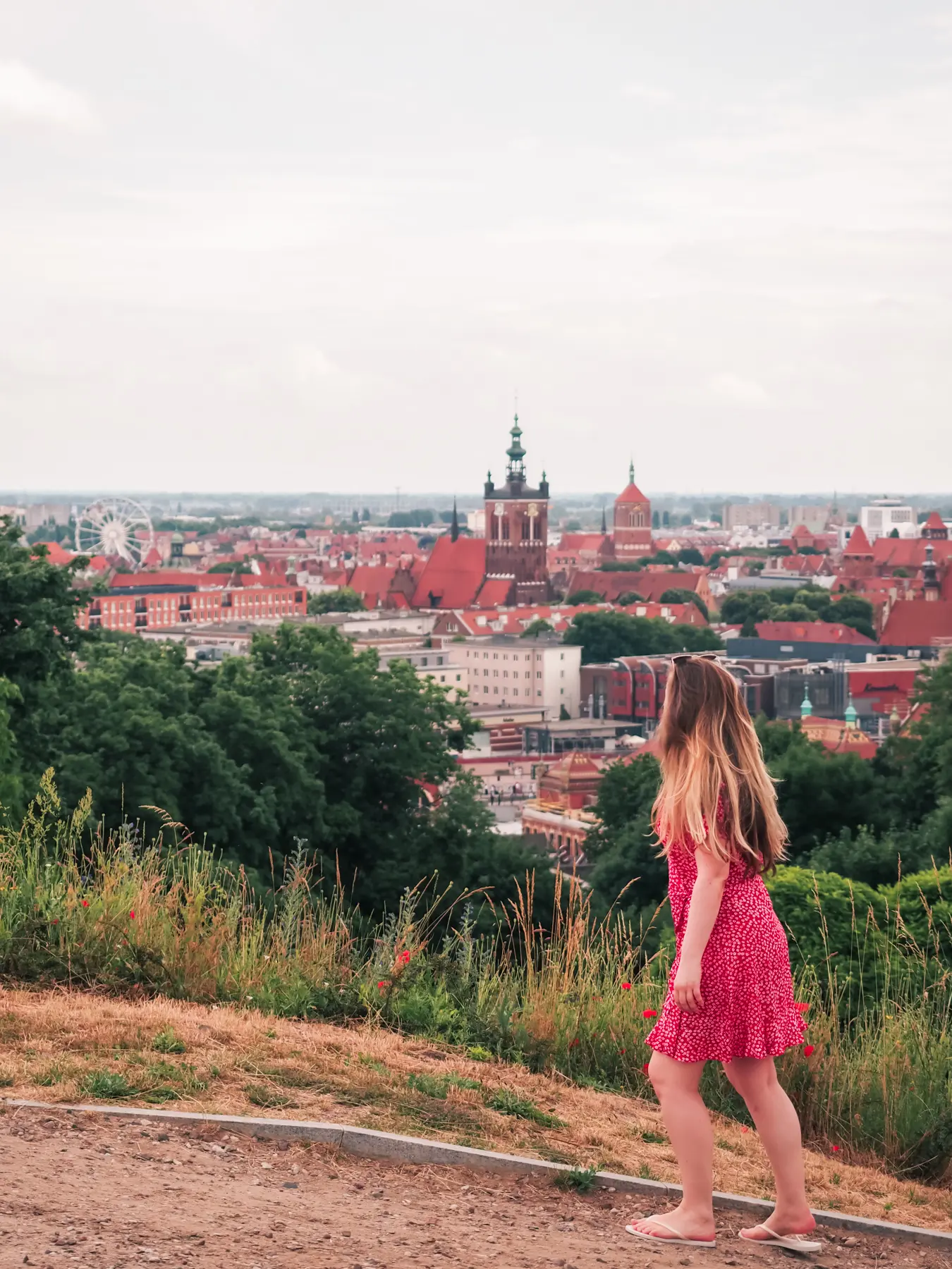 Girl in a red dress walking up the lush Gradowa Hill looking out over the rooftops of Gdansk, during a 2-day Gdansk itinerary.