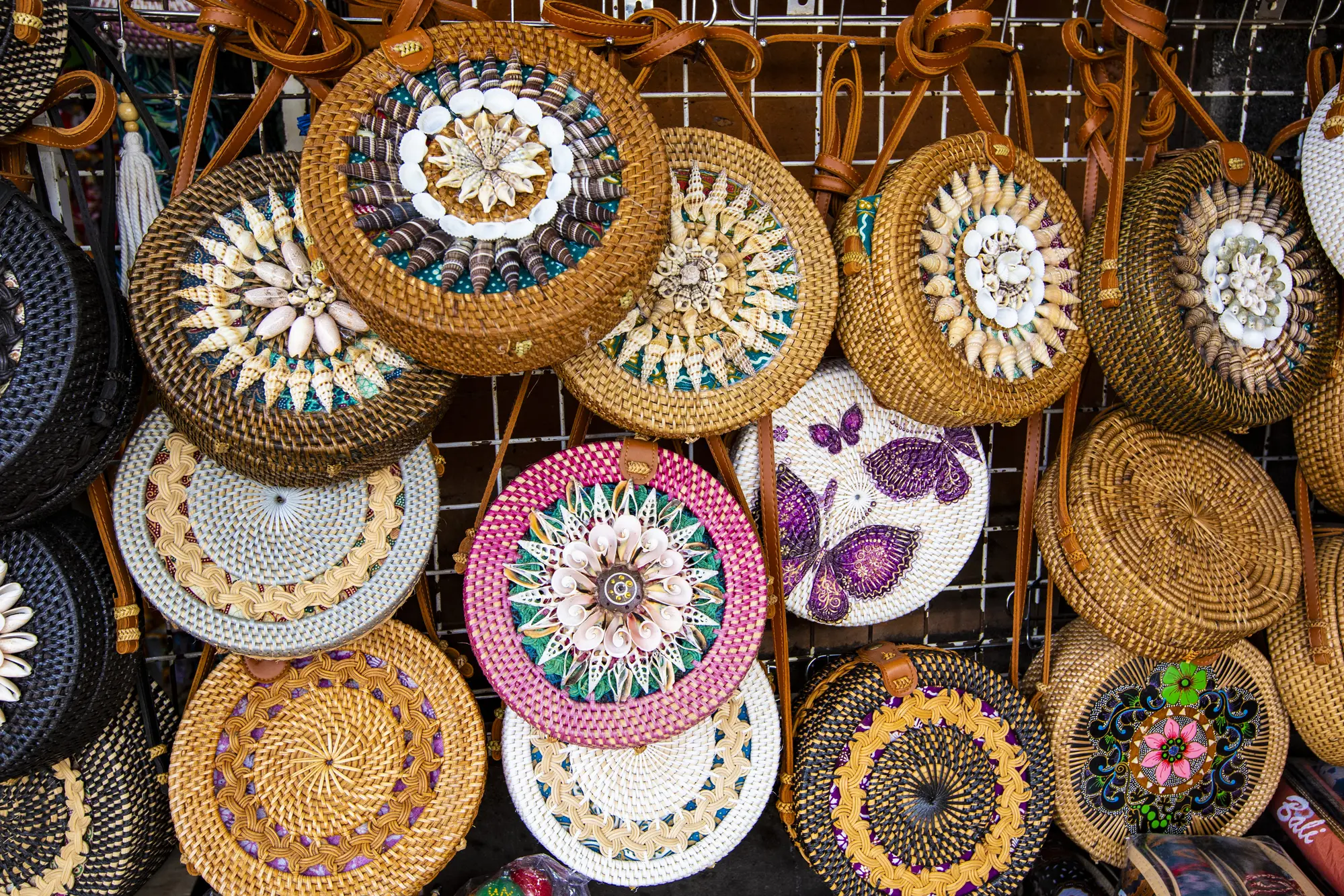 A wall of round rattan bags in different colors with seashells at Ubud Art Market, one of the most popular markets in Bali.