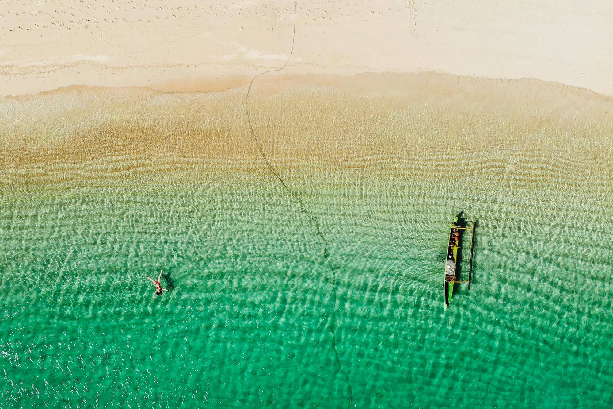 Drone shot of a girl and boat floating in green water at Tanjung Aan Beach, one of the best beaches in Kuta Lombok.