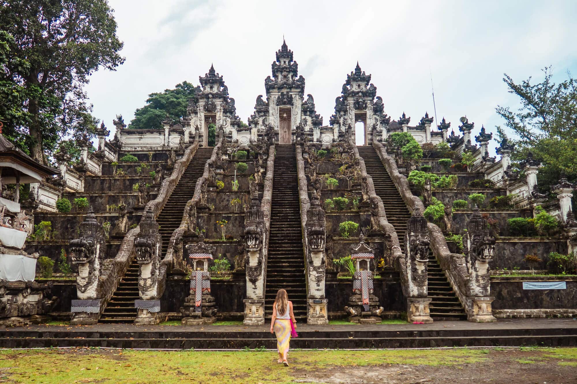 Woman wearing a pink and yellow sarong walking towards a large and ornate set of stair made from stone at Pura Lempuyang Temple, one of the top things to do Bali.