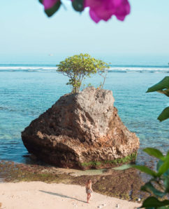 The ultimate 2 week Bali itinerary - Woman standing next to a large rock during sunrise at Padang Padang beach, one of the best beaches in Uluwatu.