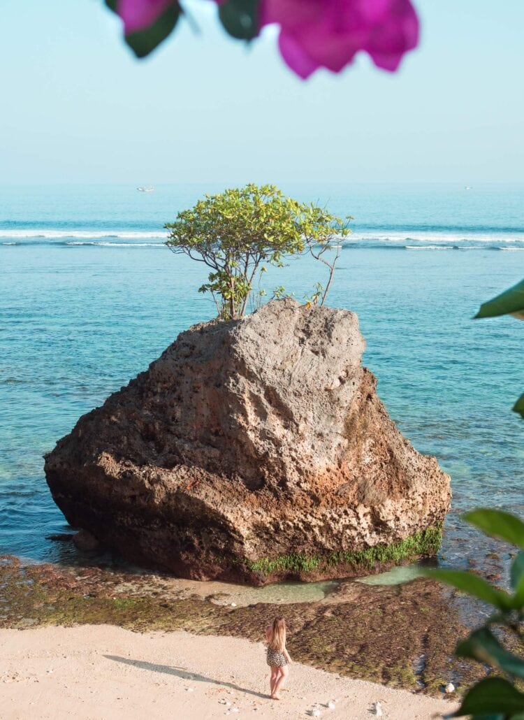 The ultimate 2 week Bali itinerary - Woman standing next to a large rock during sunrise at Padang Padang beach, one of the best beaches in Uluwatu.