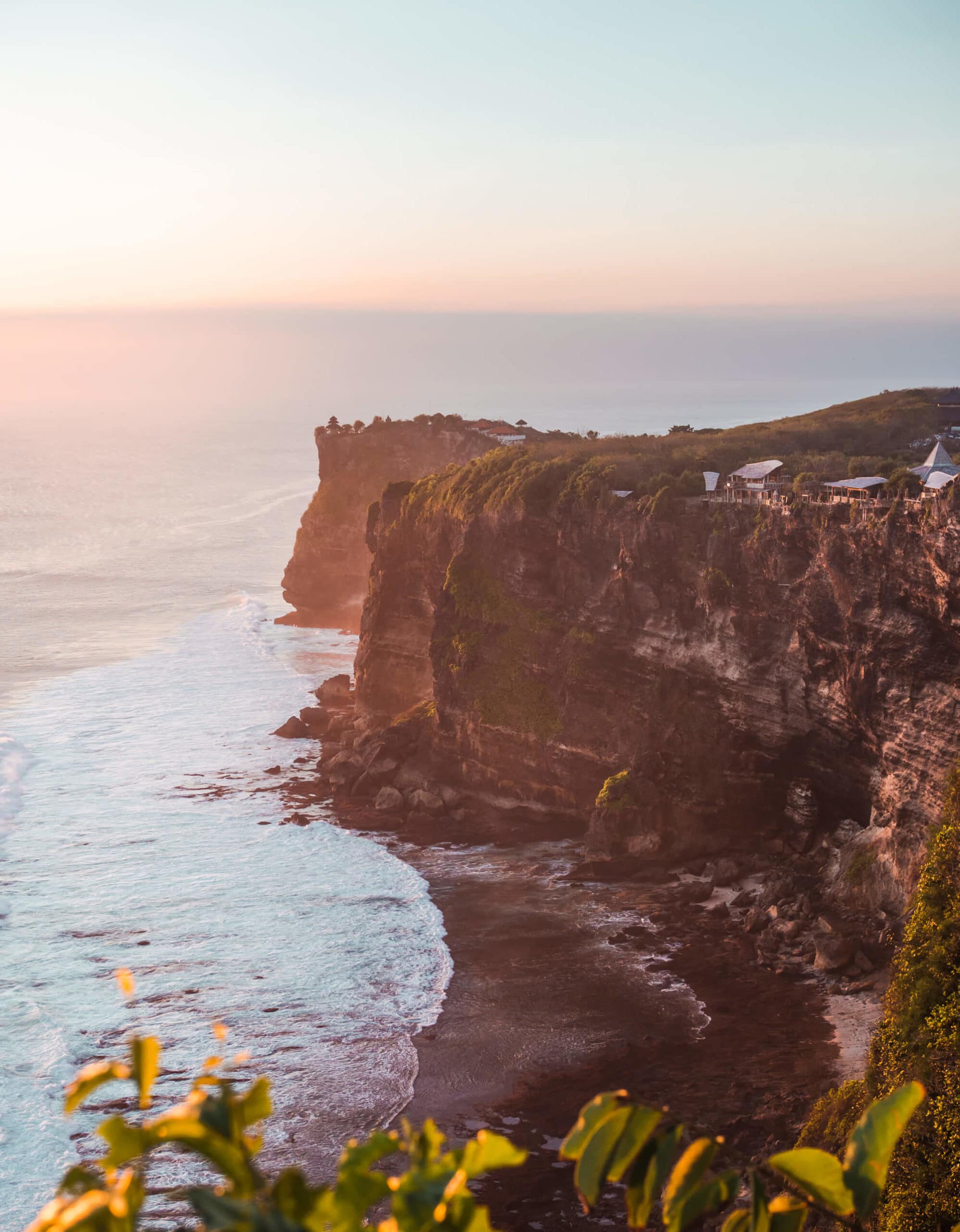 Light, pastel colored sunset over the towering Karang Boma Cliff in Uluwatu, a must on any 2 week Bali itinerary.