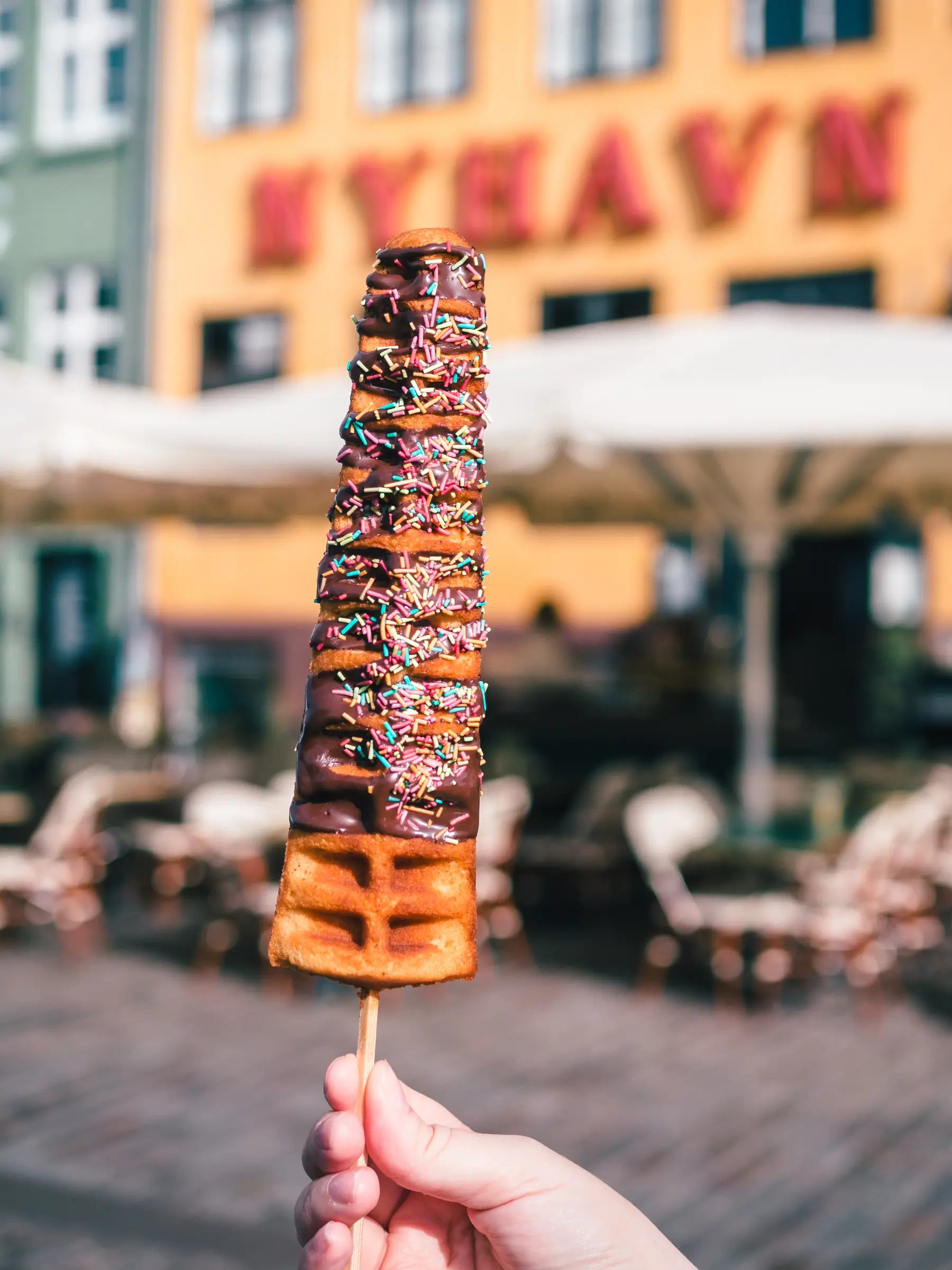 Waffle on a stick in front of the colorful buildings of Nyhavn in Copenhagen, a must on any Denmark Bucket List