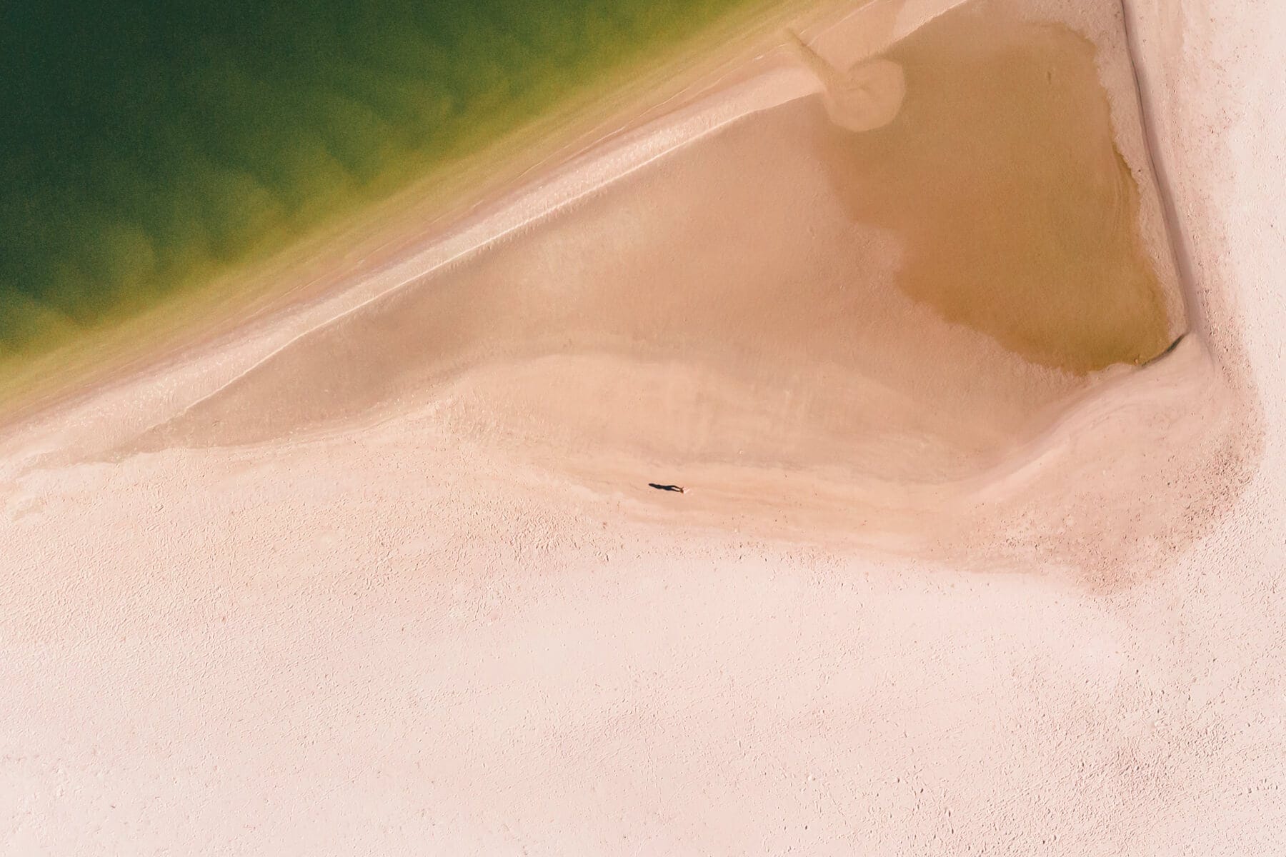 Drone shot of a small person standing on River Mouth Beach next to green water, one of the top things to do in Noosa Australia.