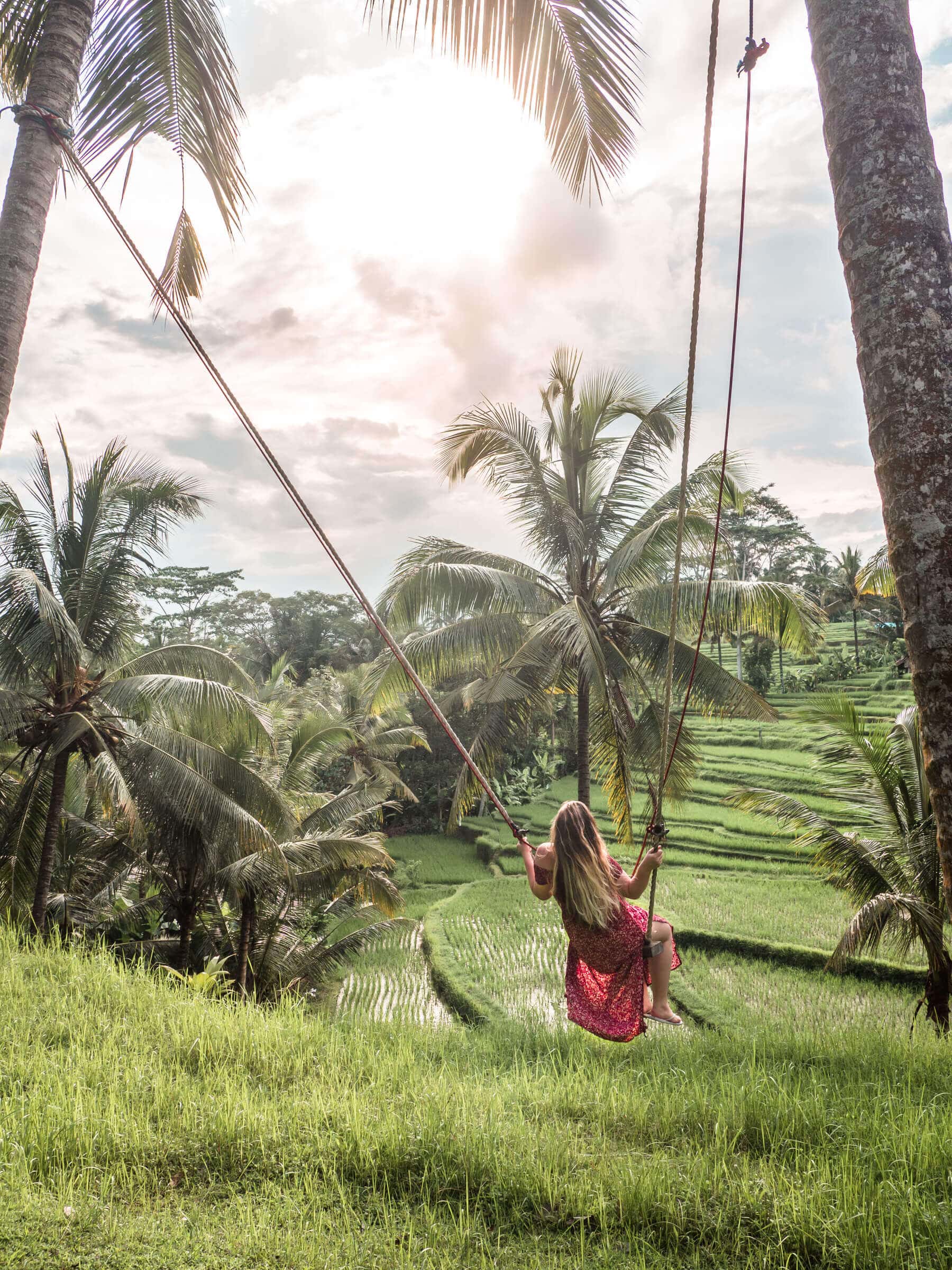 Girl in a red dress on a swing in our garden overlooking the rice fields in Sebali, Ubud. Bali swing captions for Instagram.