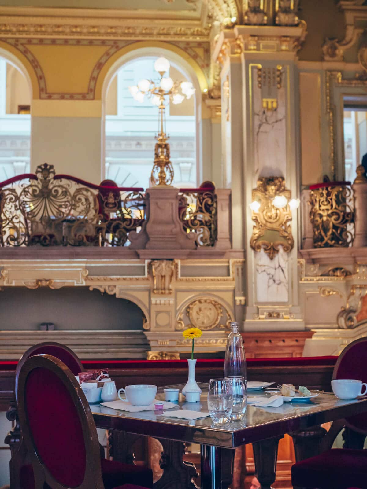 A table and red velvet chairs inside the opulent New York Café in Budapest.