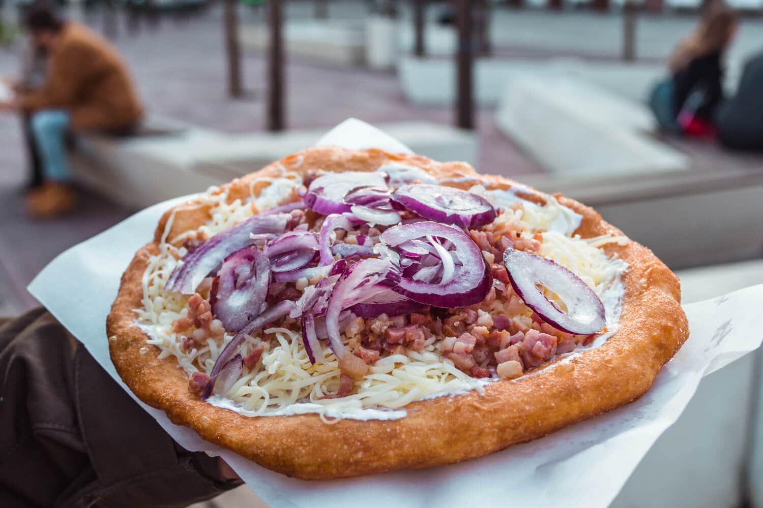 Eating Langos street food in Budapest - Fried bread topped with sour cream, cheese, red onion and bacon