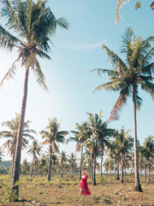 Girl in a red dress walking in a field of tall palm trees next to Tanjung Ann Beach, one of the top things to do in Lombok.