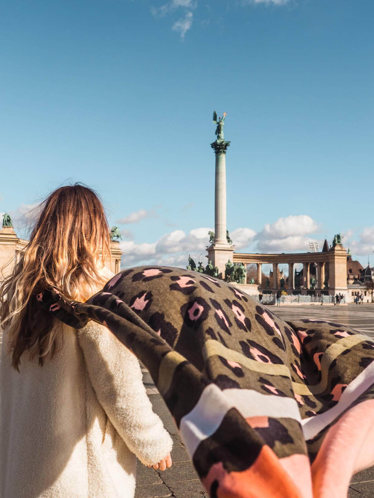 Example of content I have created as a travel content creator. Girl in a white coat with a green and pink scarf flowing towards the camera in Budapest.