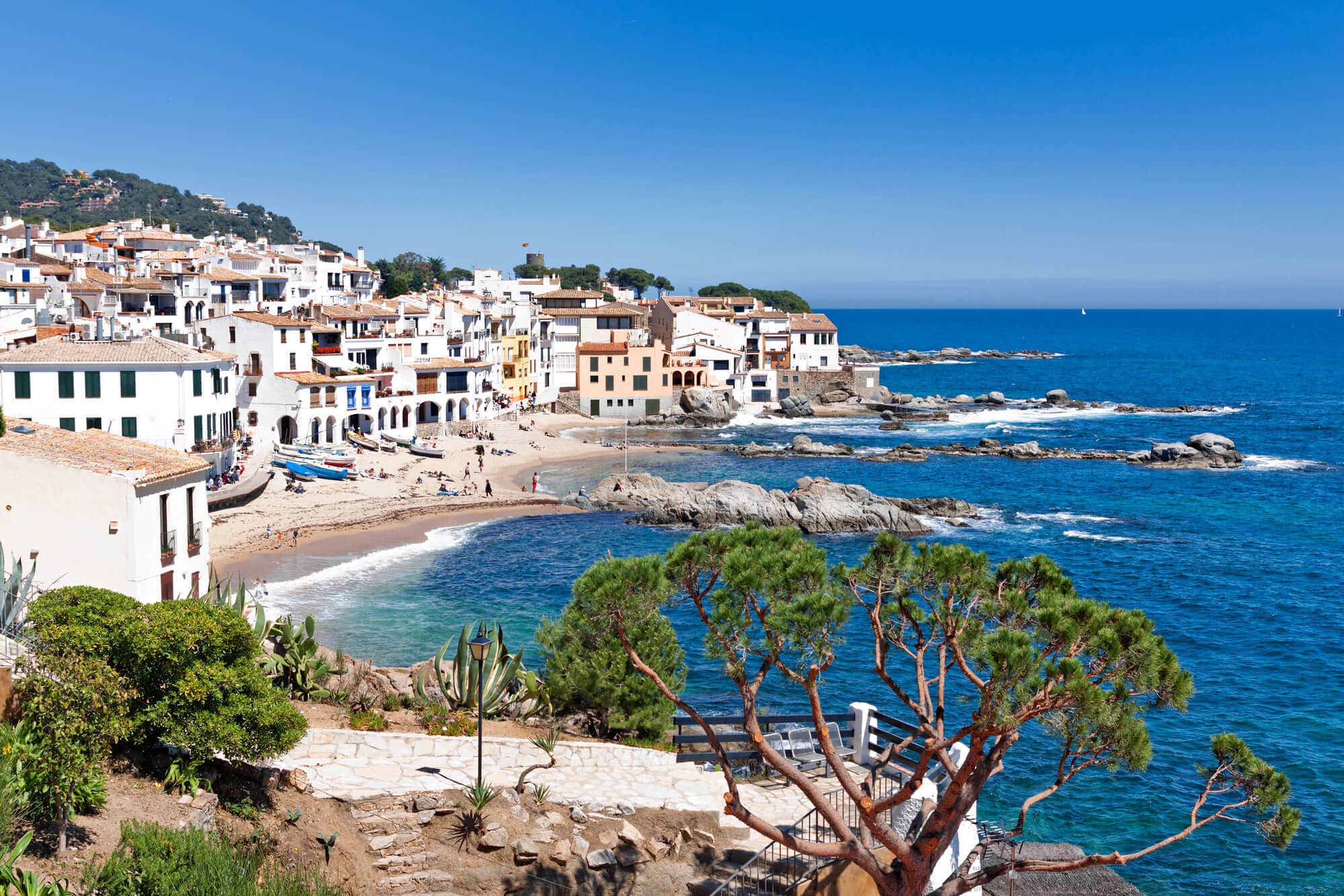 View of the beaches and white houses of Calella de Palafrugell on a sunny, clear day - One of the prettiest towns and hidden gem in Spain