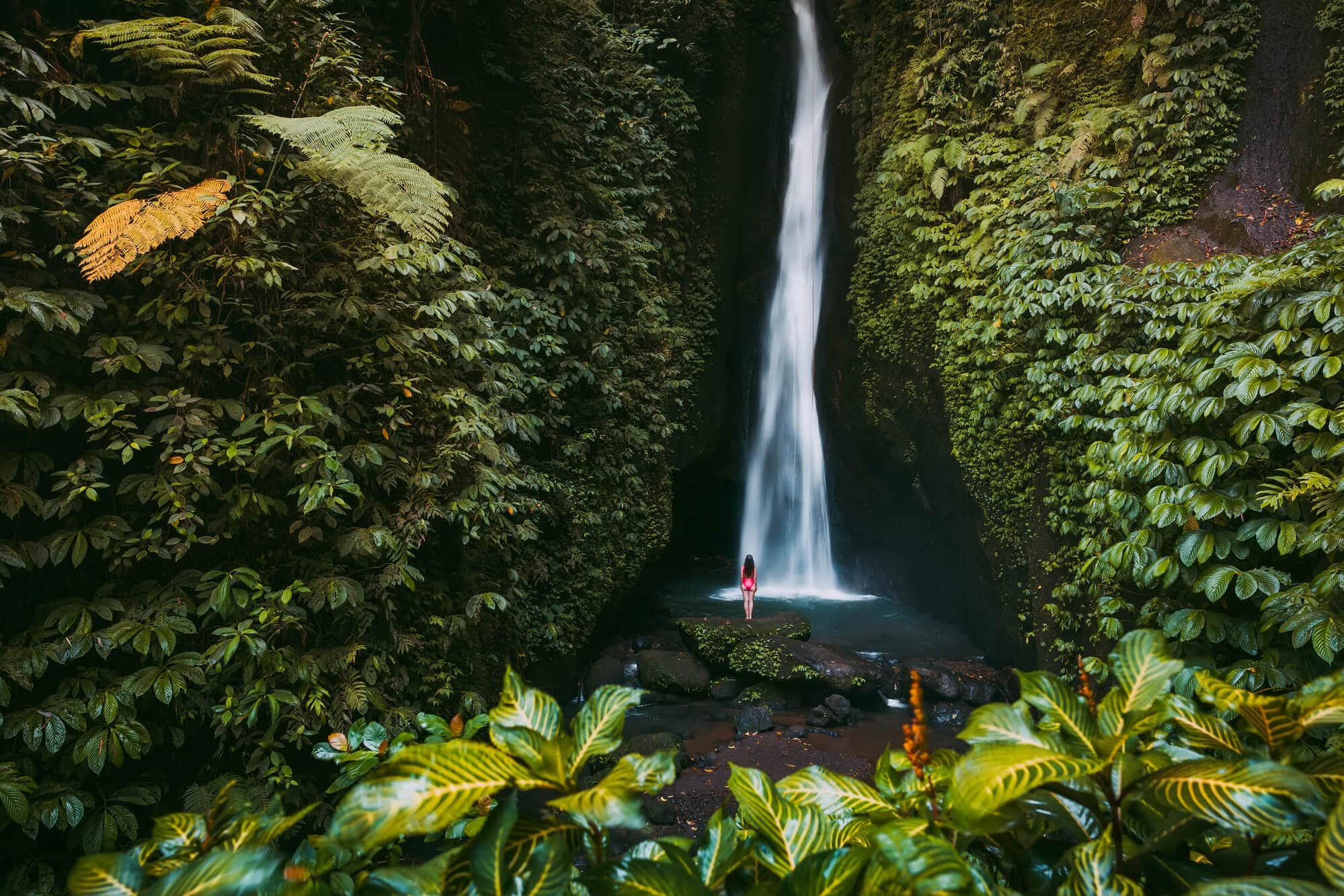 A guide to all the best waterfalls in Ubud Bali - A girl standing on a rock looking up at Leke Leke Waterfall