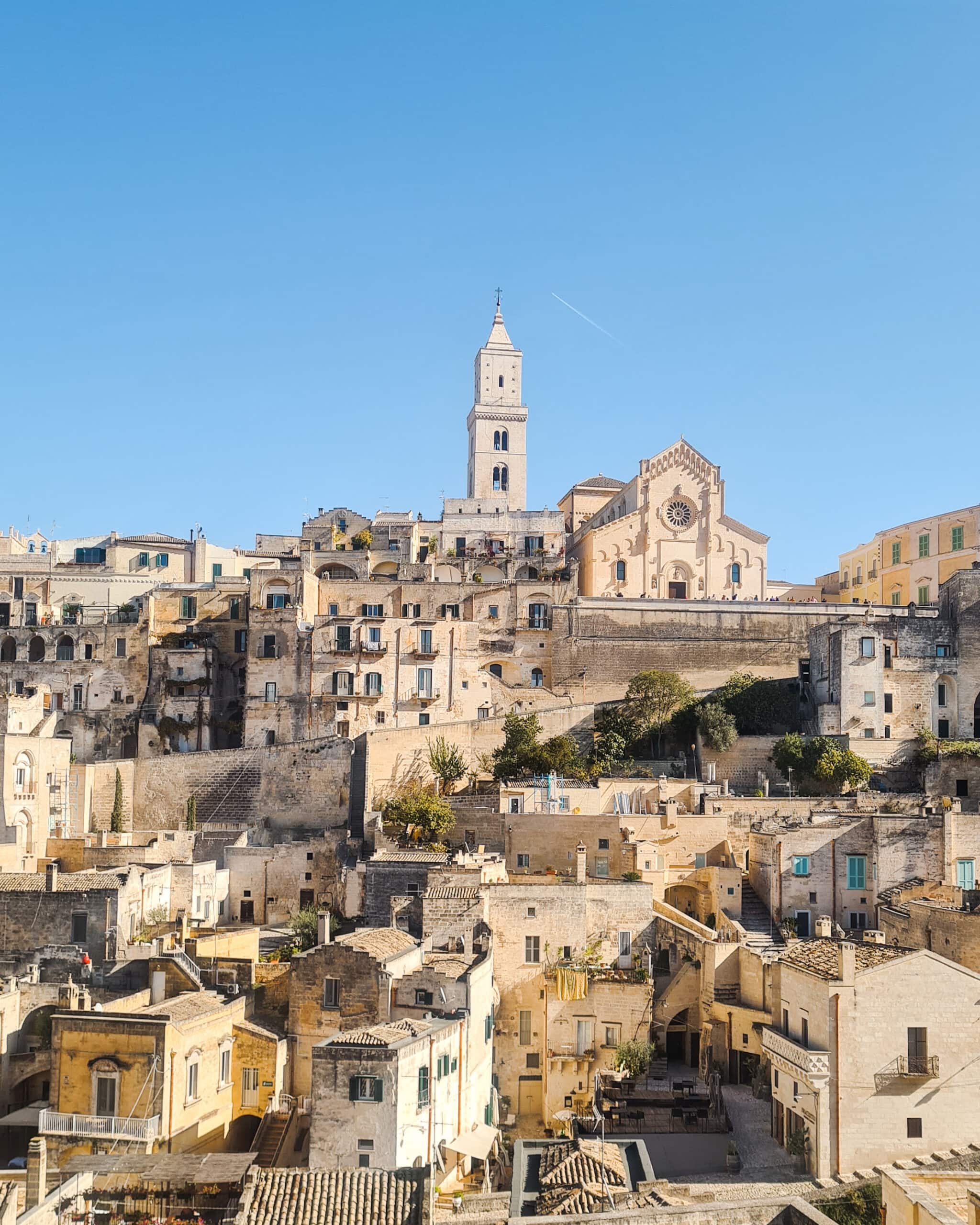 The stone town of Sassi Di Matera witch a church at the center set against a blue sky - The best hotel view in Matera