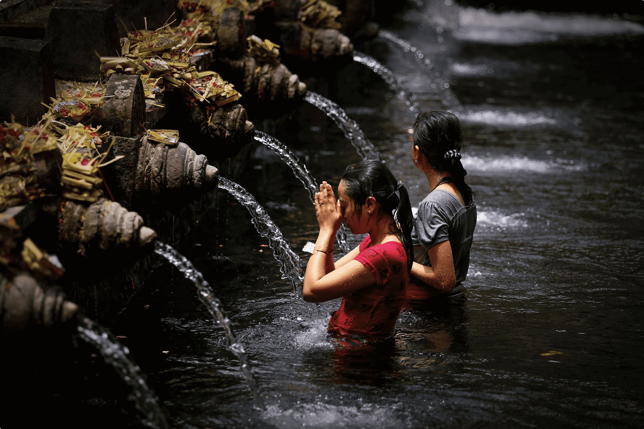 Two Balinese women bathing in the holy spring water at Tirta Gangga, join a healing tour one of the more unusual things to do in Ubud Bali