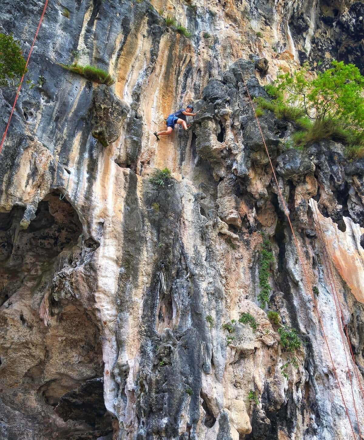 Rock climber high up on a vertical cliff during a climbing tour in Krabi, Thailand.