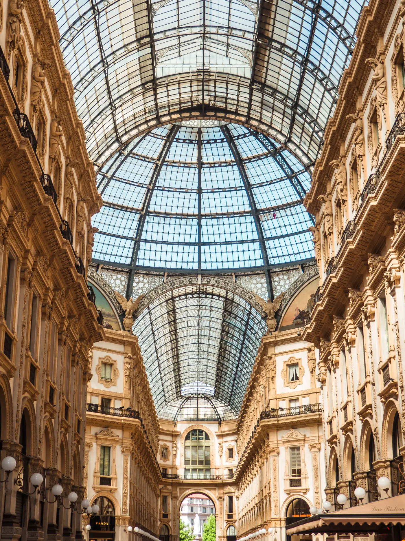 View from below of the intricate glass ceiling and beige stone walls of Galleria Vittorio Emanuele II, a must during your 2 days in Milan.