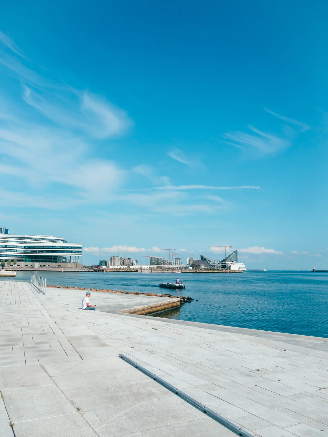 Man sitting on a modern pier looking out over the blue ocean on a sunny day, during two days in Aarhus Denmark.