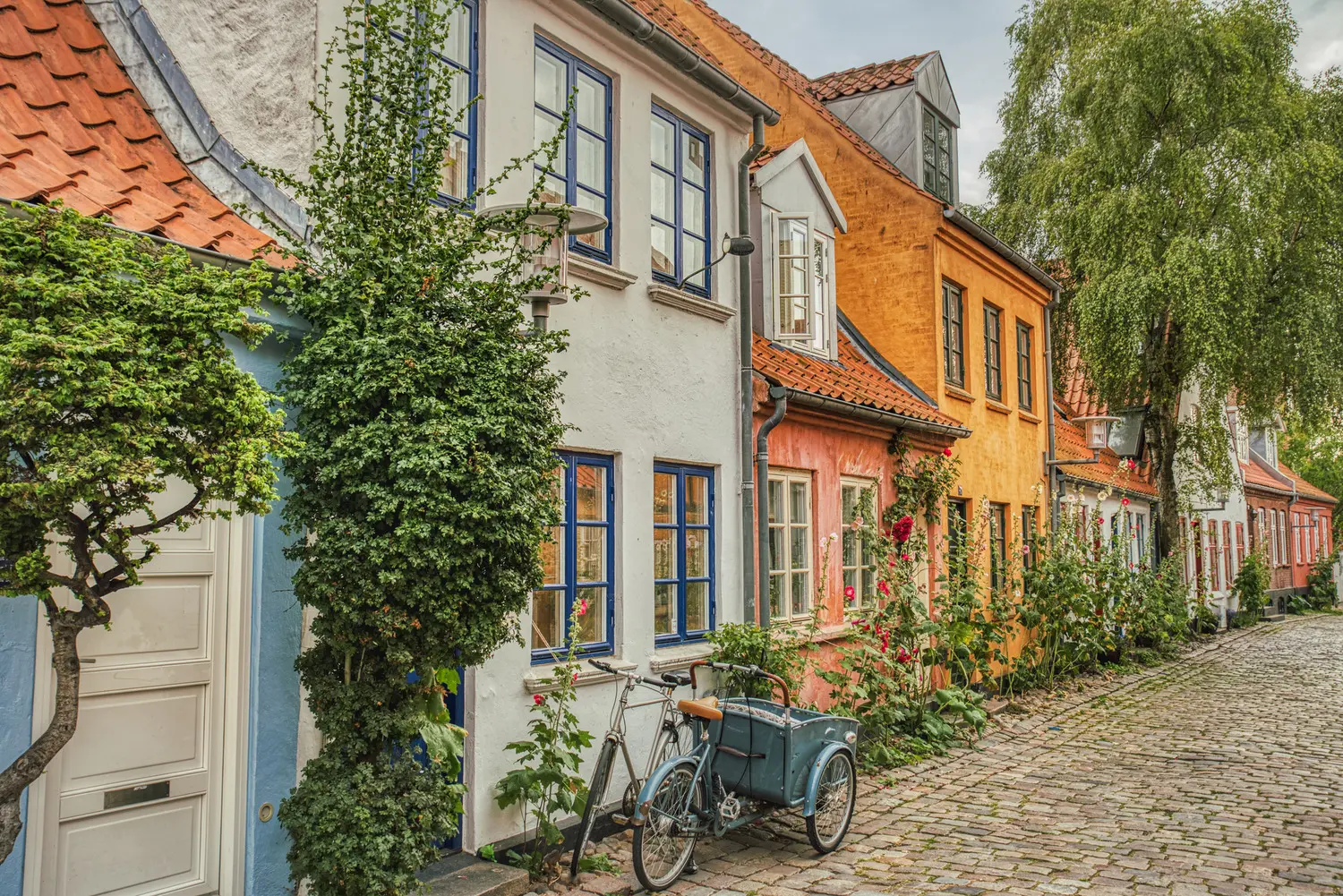 Blue retro tricycle parked outside a row of small colorful houses along the cobbled M&oslash;llestien street, a hidden gem in Aaurhus. 