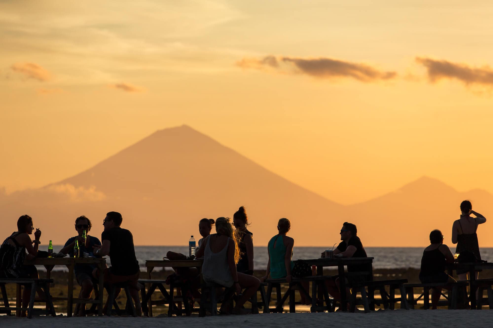 People enjoying an orange sunset at Gili T with Bali's Mount Batur in the background.