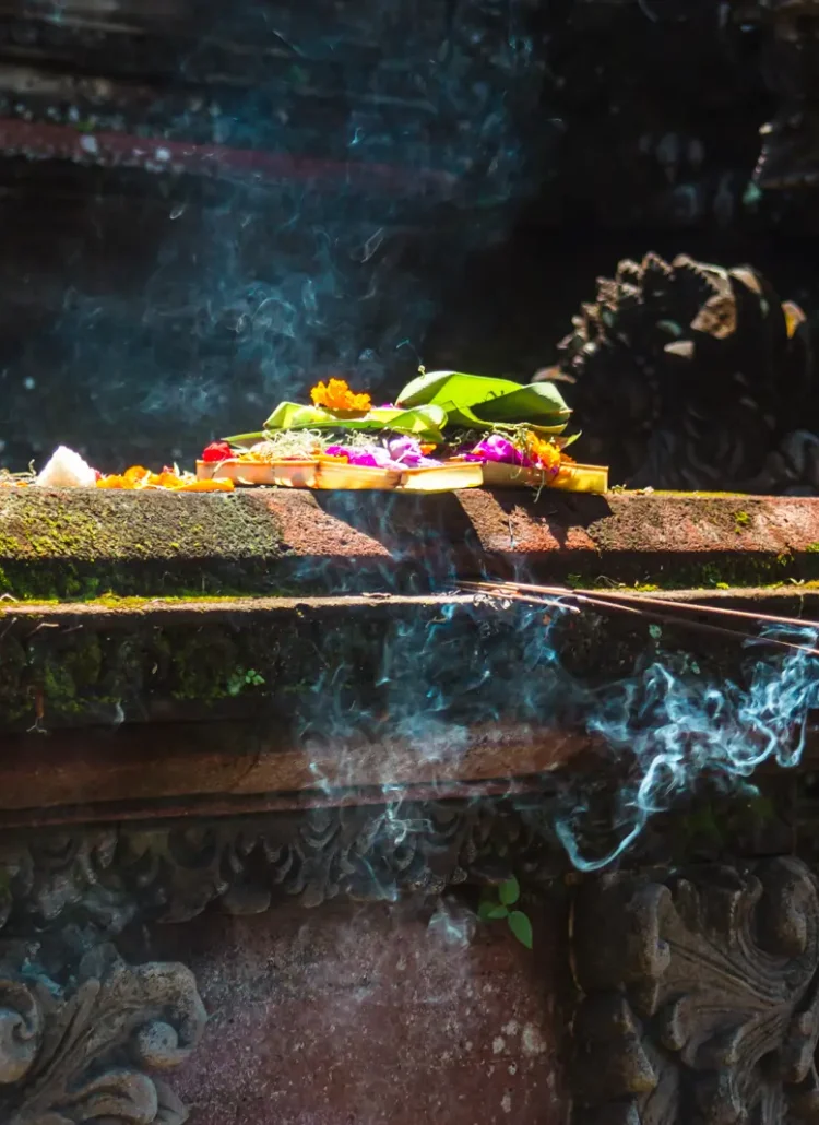 Close up of Balinese offering with flowers and incense in a basket on an ornate stone table in a temple, things to know before going to Bali.