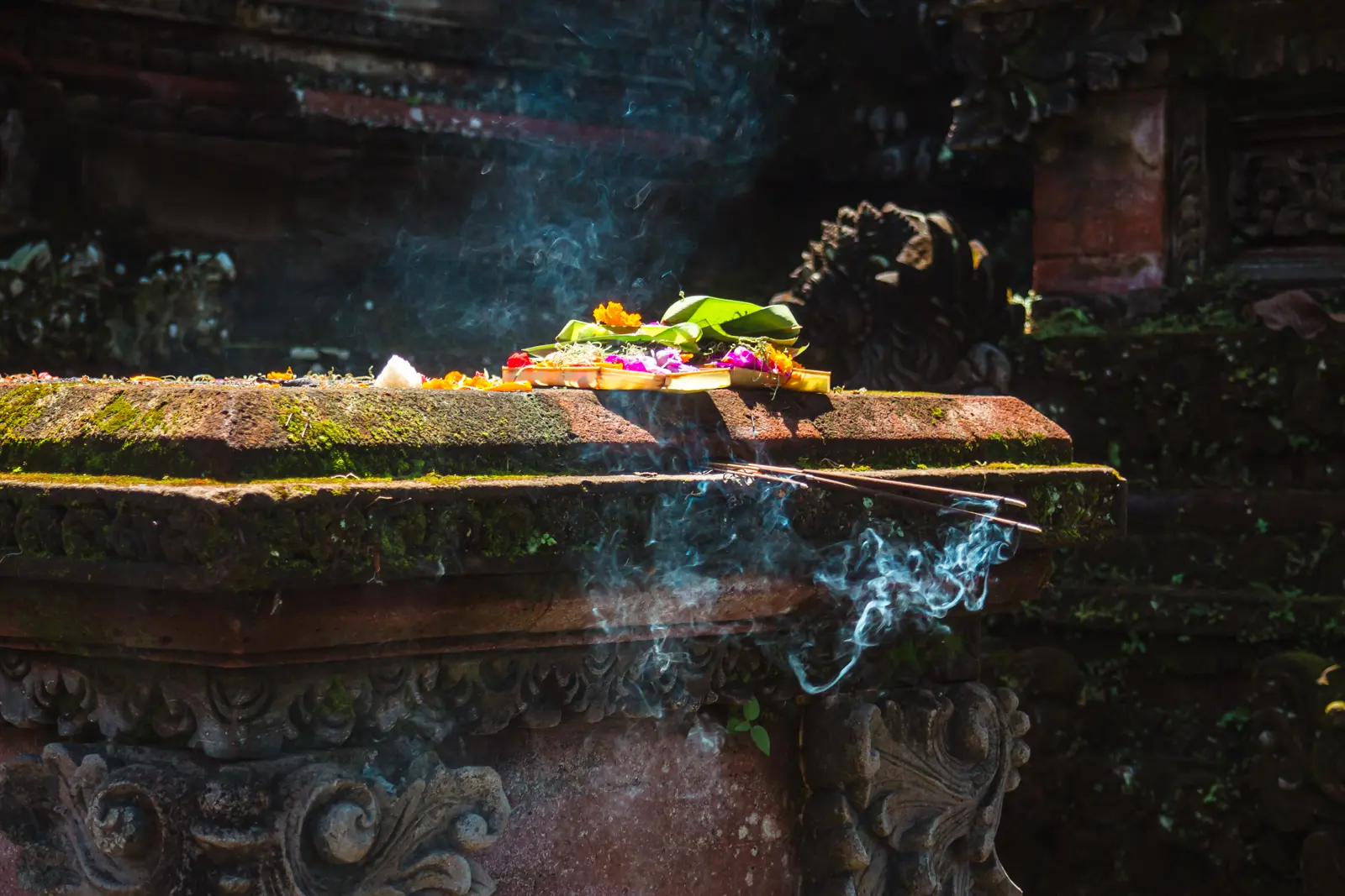 Close up of Balinese offering with flowers and incense in a basket on an ornate stone table in a temple, things to know before going to Bali.