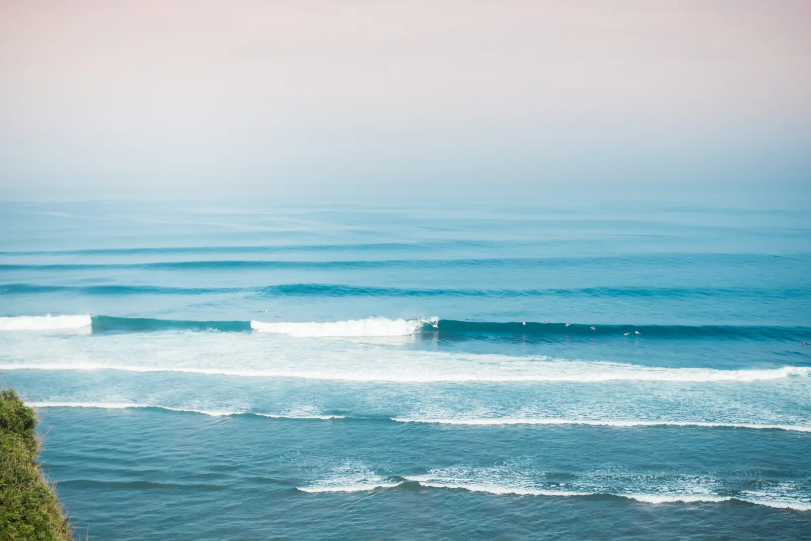 Looking out at the ocean and a surfer on a wave from the cliff in Uluwatu during sunrise, things to know before going to Bali.