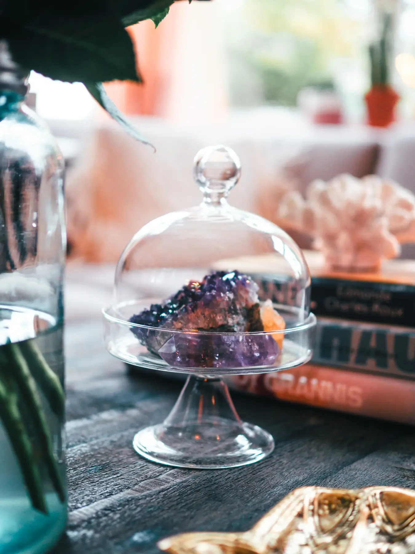 Manifest your dream boho house and decor, close up of crystals on display in a glass cloche, travel coffee table books.