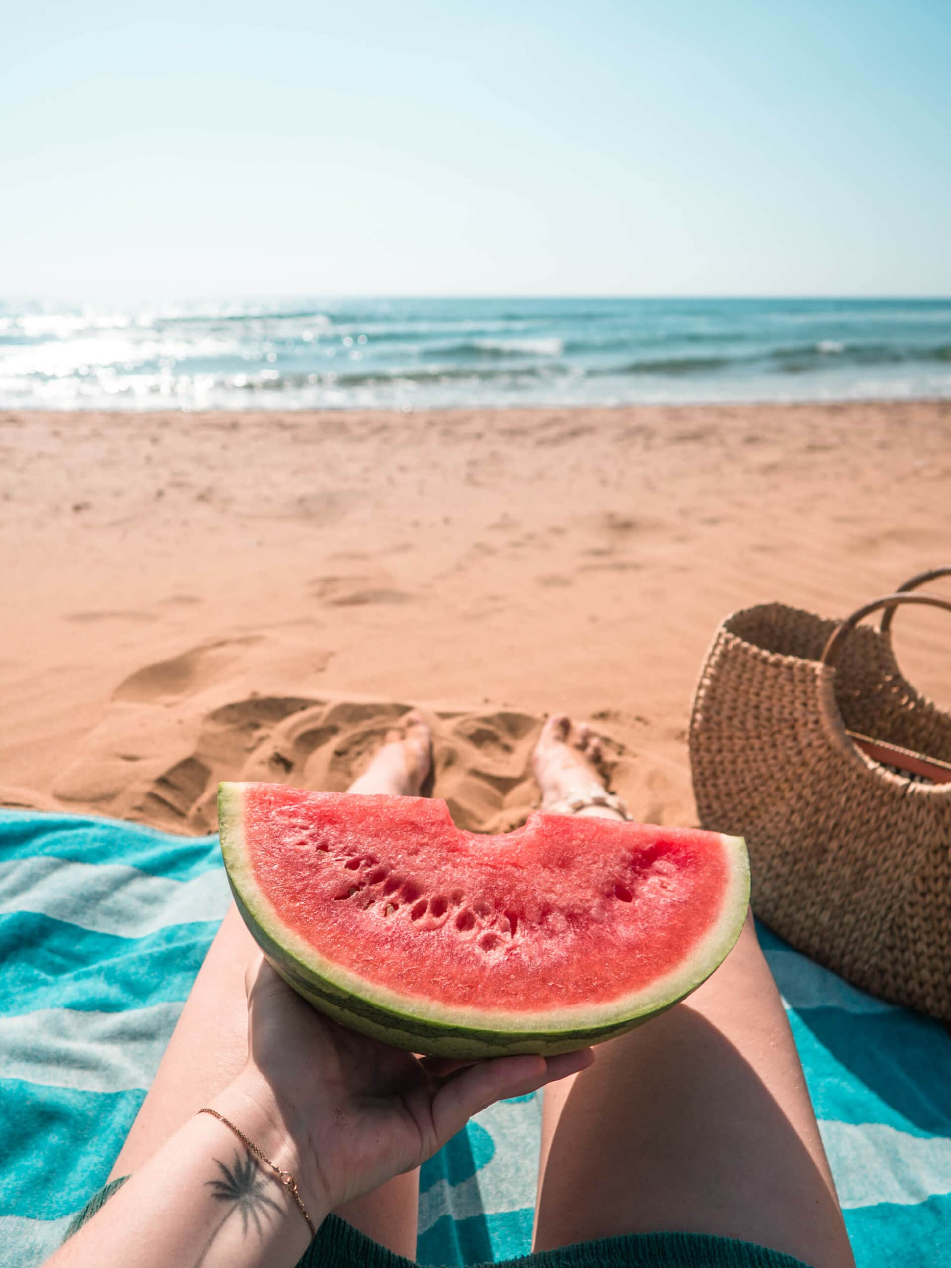 Girl sitting on a turquoise towel in the sand holding a piece of watermelon at Playas Calblanque just outside Cartagena in Spain
